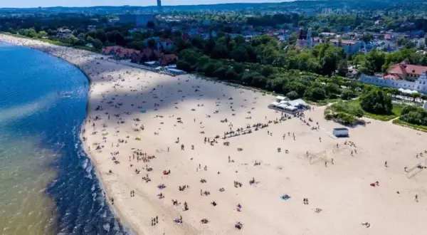 Plaża w Sopocie, do którego miast nad morzem można dojechać pociągiem z Warszawy. Tłumy ludzi odpoczywają na piasku.