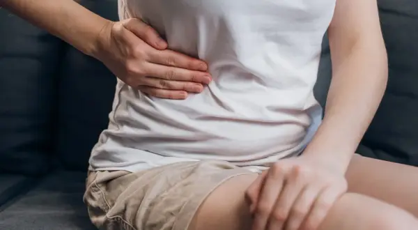 Osoba trzyma się za prawy bok, gdzie znajduje się wątroba. Czy witamina B3 może pomóc w jej dolegliwościach?