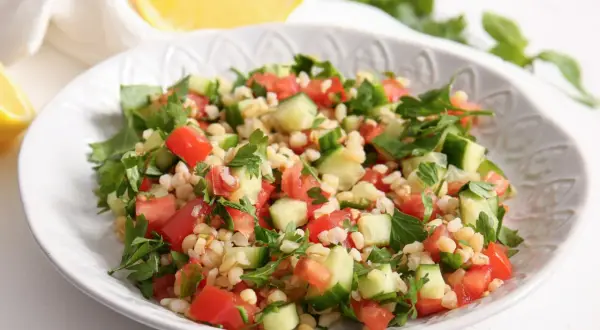 Orzeźwiająca sałatka z kaszą bulgur, pomidorami, ogórkiem i natką pietruszki, podana na białym talerzu.