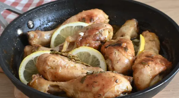 Cosce di pollo al limone succulente e dorate, cotte in padella con fette di limone e erbe aromatiche.