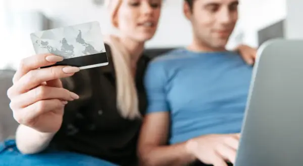 Kobieta trzyma kartę, mężczyzna pracuje na laptopie. Dane karty i PESEL to kluczowe informacje, jakie dane są potrzebne do wyłudzenia kredytu.