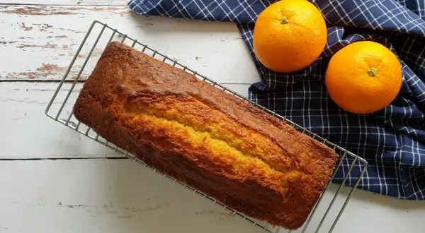 Gâteau doré sur grille, prêt à être dégusté. Une recette gâteau facile et originale, avec des oranges fraîches à côté.