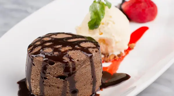 Un fondant au chocolat cœur coulant, servi avec une boule de glace à la vanille, une fraise et un coulis de fruits rouges.