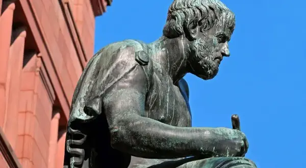 Posąg filozofa, który zgłębia tajniki bytu i ontologii, siedząc z piórem w dłoni.