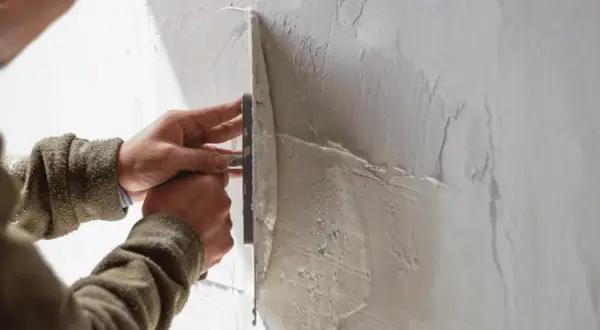 Mani esperte stendono il rasante su un muro, creando una superficie liscia e uniforme.