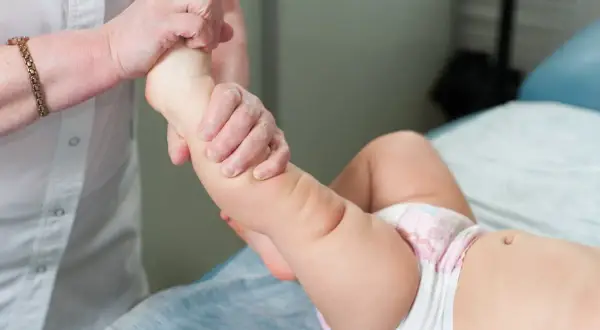 Mani esperte muovono la gamba di un neonato, un gesto di cura per l'ipotonia muscolare neonato.