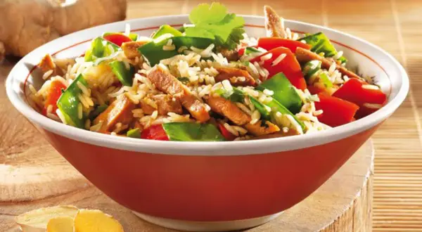 Schüssel mit Reis, Fleischstreifen, Paprika und Erbsen. Ein köstliches Gericht aus der Wok-Küche, garniert mit Koriander.