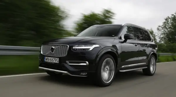 Czarne Volvo XC90 V8 pędzi po drodze, rozmazane drzewa i krajobraz świadczą o dużej prędkości.