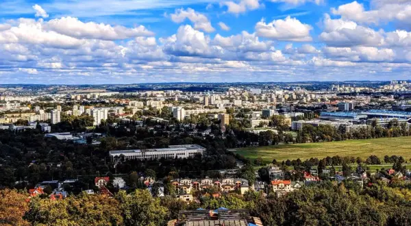 Widok na rozległe osiedla Krakowa, gdzie ceny mieszkań mogą być wysokie. W oddali widać zabudowania i zieleń.