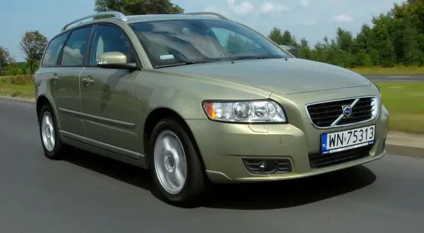 Złoty Volvo V50 1.6 diesel w ruchu drogowym, z zielenią drzew w tle.