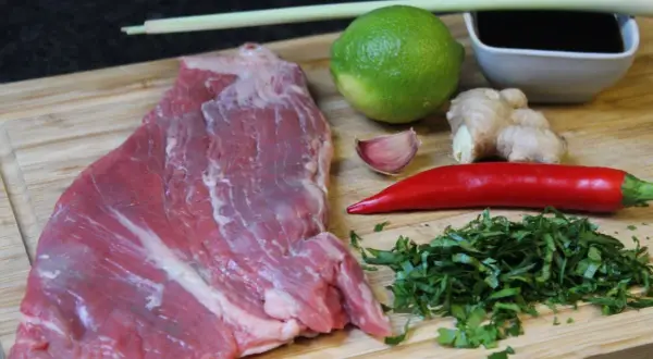 Rohes Rindersteak liegt bereit, um mit Limette, Ingwer, Chili, Knoblauch und Kräutern mariniert zu werden.