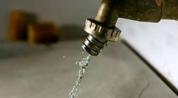 Un robinet en laiton coule, projetant un jet d'eau. Des éponges floues sont visibles en arrière-plan. Il est temps d'avoir plus d'eau dans la maison.