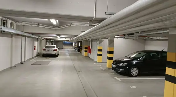 Wrocław główny parking cennik: podziemny parking z białym i czarnym Volkswagenem, białym BMW, rurami i klimatyzacją.