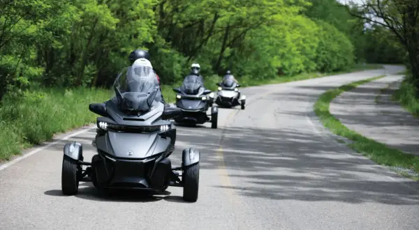 Trzy pojazdy typu Can-Am Spyder jadące po krętej drodze wśród zieleni. Ich dynamiczny wygląd podkreśla **efekt shimmy** podczas jazdy.