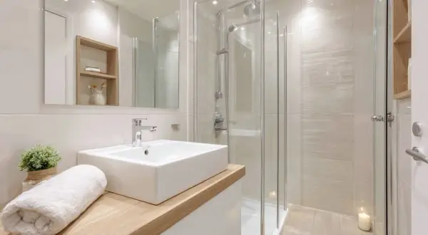 Une petite salle de bain moderne avec une douche vitrée, un lavabo rectangulaire sur un meuble en bois clair, et une serviette blanche pliée.