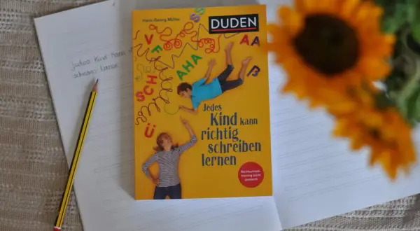 Ein Duden-Buch mit dem Titel "Jedes Kind kann richtig schreiben lernen" liegt auf einem Notizbuch. Ein Bleistift liegt daneben. Rechtschreib-training leicht gemacht.