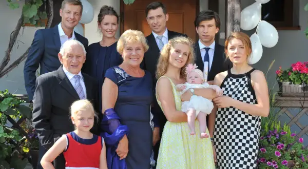 Rodzina z serialu "M jak miłość" pozuje do zdjęcia. Wszyscy uśmiechnięci, w tle balony i kwiaty.