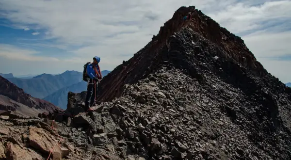 Alpinista na grani, zbliża się do najwyższego szczytu Gruzji. W tle pasmo górskie.