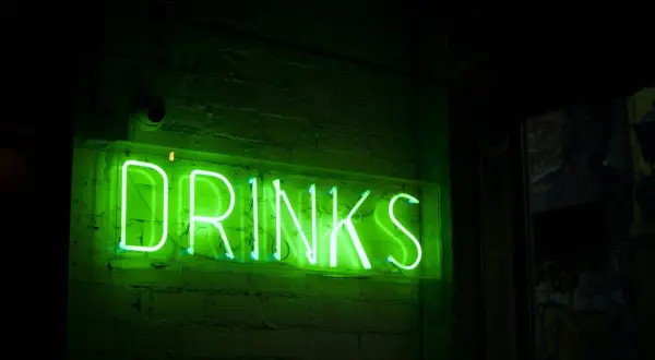 Zielony neon "DRINKS" na ceglanej ścianie. Czas na drinka, jakim alkoholem jesteś?