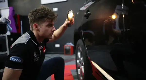 Detailer używa lampy, by ocenić stan lakieru. Widać drobne niedoskonałości na czarnym samochodzie.