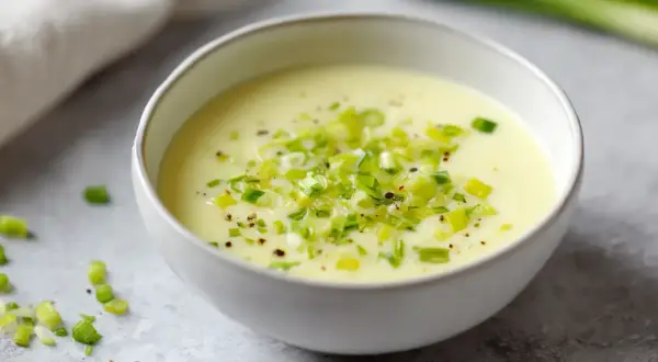 Un bol de fondue de poireaux crémeuse, garnie de poireaux frais hachés et de poivre noir.