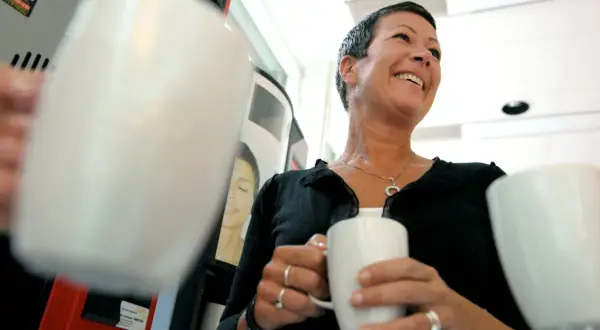 En kvinna ler glatt med en kaffemugg i handen. Hon verkar njuta av stunden, vilket visar vad betyder inflytande i vardagen.
