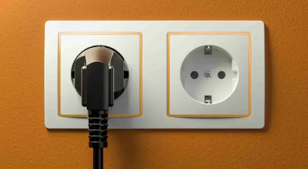 Dwa gniazdka elektryczne, jedno z wtyczką, na pomarańczowej ścianie. Typowe gniazdka w Turcji.