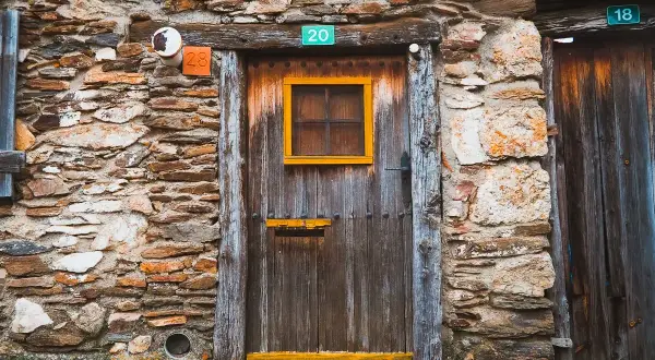 Puerta de madera rústica en una pared de piedra en la serrada de la fuente. Números 20, 28 y 18 adornan la entrada.