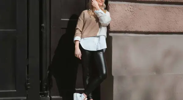 Styling-Tipp: So kannst du lederleggings kombinieren. Eine Frau mit blonden Haaren trägt sie mit einem weißen Hemd und einem zweifarbigen Pullover.