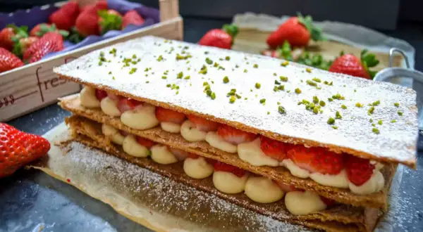 Ein köstliches Mille-feuille mit frischen Erdbeeren und Sahne, bestreut mit Puderzucker und Pistazien.