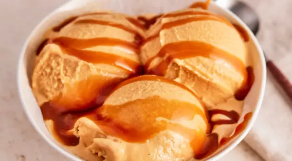 Drei Kugeln cremiges Karamell-Eis, übergossen mit flüssigem Karamell, in einer weißen Schüssel.