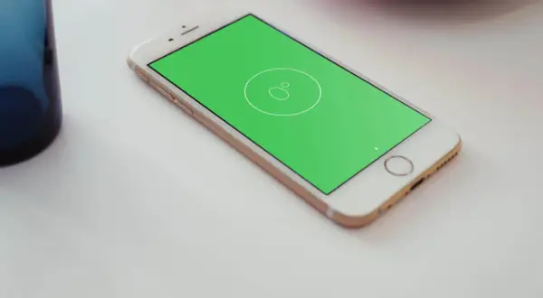 Złoty telefon z zielonym ekranem, na którym widnieje ikona poziomicy. Obok stoi niebieska szklanka.