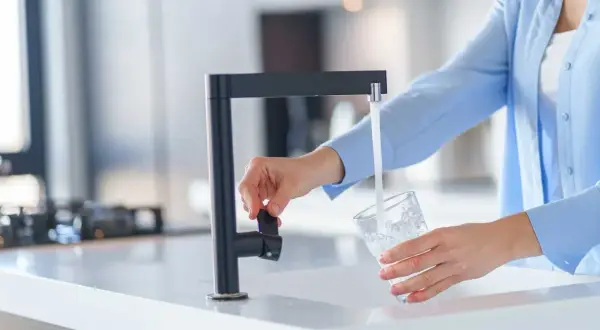Une personne remplit un verre d'eau du robinet, peut-être pour tester la dureté de l'eau.
