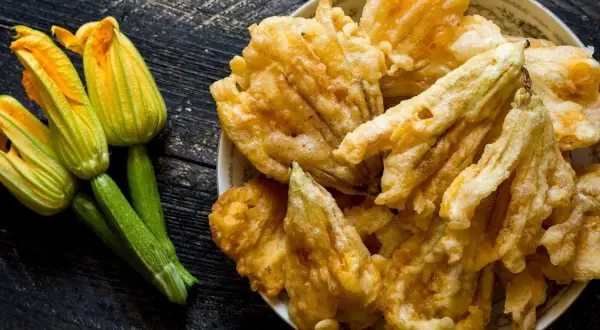 Flores de calabacín frescas y doradas flores de calabacín rebozadas en un plato.