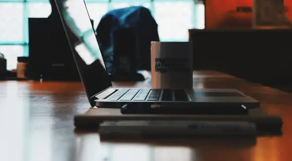 Laptop na drewnianym stole, obok kubek. Zastanawiasz się, jak wygasić ekran w laptopie?