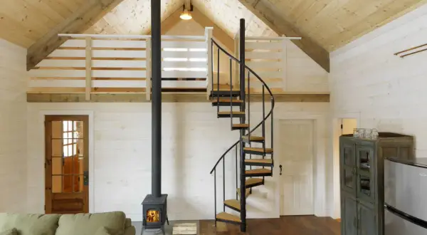 Idee soppalco basso: scala a chiocciola in metallo e legno porta a un soppalco con ringhiera in legno, stufa a legna e divano.
