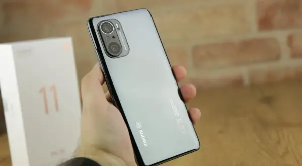 Dłoń trzyma błyszczący telefon Xiaomi 11i z potrójnym aparatem. Obok stoi białe pudełko z cyfrą 11.