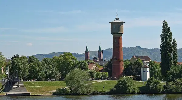 Wasserturm und Kirchtürme über grünen Bäumen, die die ladenburg altstadt säumen, mit Fluss im Vordergrund.
