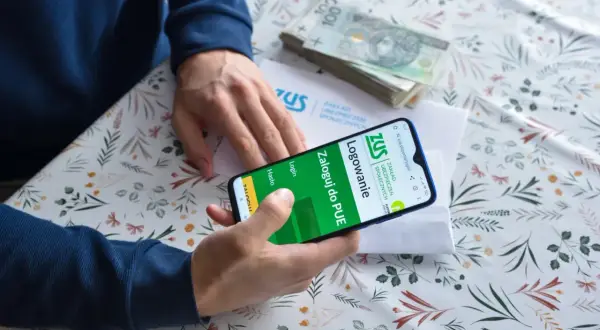 Słuchacz szkoły policealnej loguje się do PUE ZUS, by sprawdzić składki. Na stole stos banknotów.