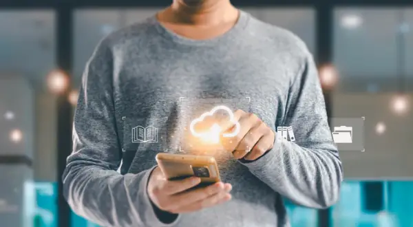 Osoba trzymająca smartfon z ikonami chmury, książki i folderów.