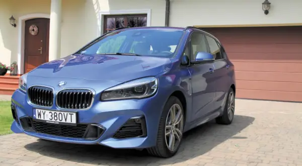 Niebieski minivan BMW serii 2 Active Tourer zaparkowany przed domem.