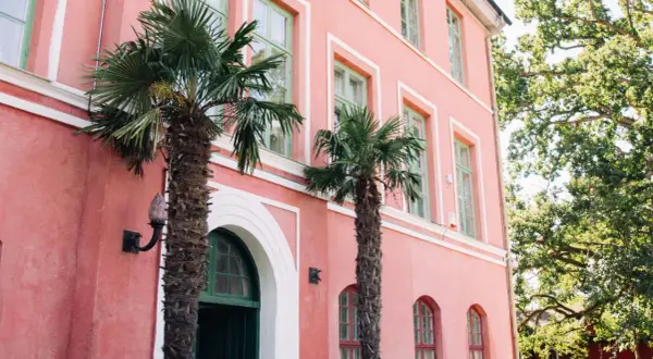 Hoby Kulle Herrgård i rosa nyanser med gröna fönster och palmer som ger en oväntad känsla.