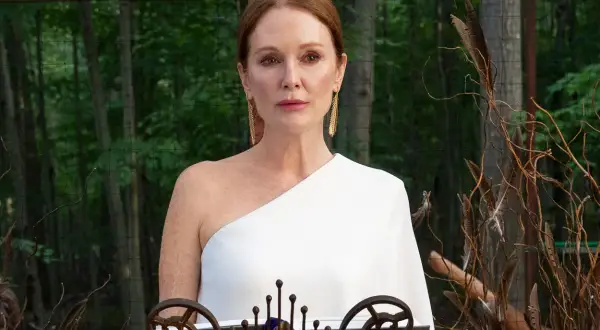 Julianne Moore i den vita klänningen i "Sirens"-serien, med en bakgrund av skog och dekorativa kvistar.