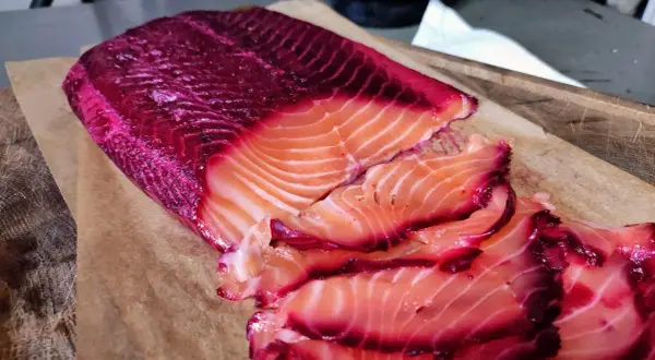 Rote Bete Lachs, mariniert und in Scheiben geschnitten, liegt auf Backpapier. Die leuchtend pinken Ränder des Lachses sind ein Blickfang.