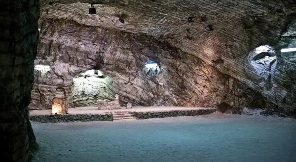 Interno della cattedrale di sale di Realmonte, con pareti rocciose stratificate e un altare illuminato.