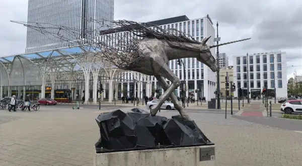 Metalowy jednorożec na skalnej podstawie, symbolizujący dynamikę i nowoczesność, na tle architektury Piotrkowska Łódź.