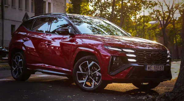Czerwony Hyundai Tucson 4 w sportowej wersji N Line zaparkowany na tle jesiennych drzew i kamienicy.