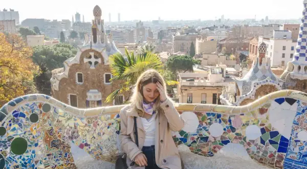 Frau sitzt auf einer bunten Mosaikbank im Park Güell, mit Blick auf Barcelona. Tolle Barcelona Tipps für deinen Besuch!