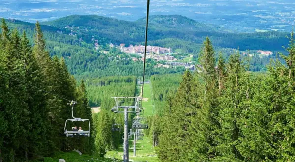 Wjazd kolejką linową na wysoką kopę szlak. Widok na zielone lasy i zabudowania w oddali.