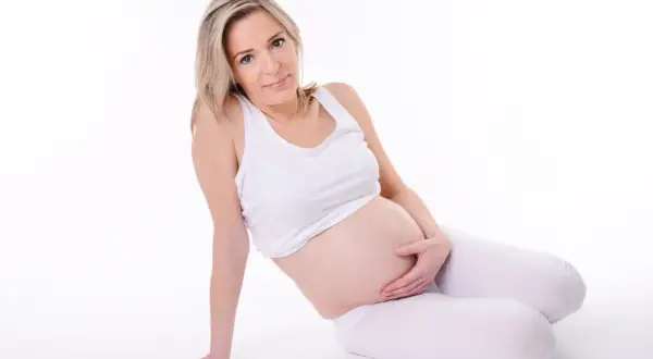 Kobieta w ciąży geriatrycznej, z dłońmi na brzuchu, siedzi na białym tle.
